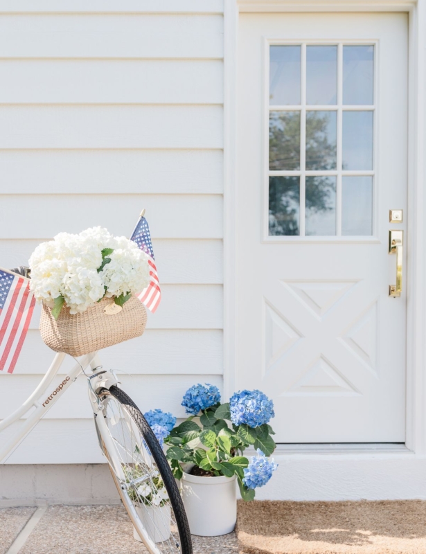 一辆白色的骑自行车装饰于7月4日,停在白色门前,带有黄铜外门把手